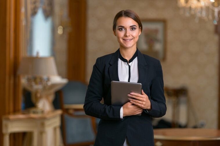 stock photo smiling businesswoman in suit standing in hotel room using digital tablet and looking camera 2280648849 transformed