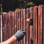 man protective gloves is painting wooden fence bright summer day 1