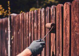 man protective gloves is painting wooden fence bright summer day 1