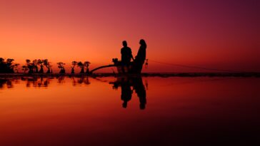 silhouette people by lake against orange sky