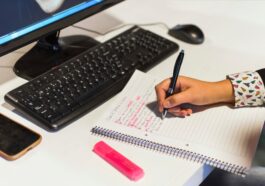 crop hand writing notebook near computer 1
